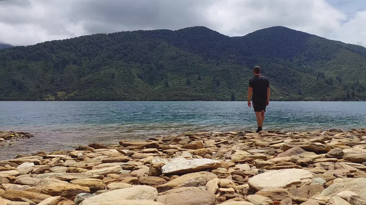 un hombre recogiendo y saltando piedras en una playa rocosa