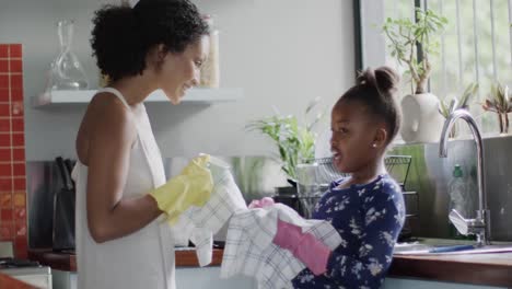 happy african american mother and daughter washing dishes in kitchen, slow motion