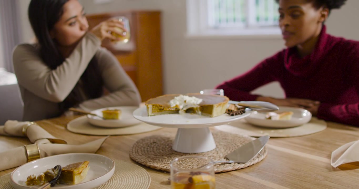 African American women sharing cake and talking at table while camera pulling back showing glass