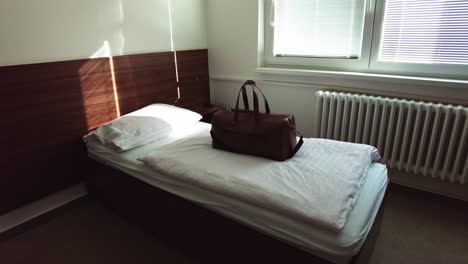 brown leather bag sits on hotel single bed in morning light from window