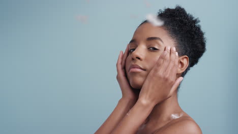 slow-motion-beauty-portrait-attractive-african-american-woman-feathers-falling-on-smooth-skin-touching-bare-shoulders-enjoying-natural-skincare-gently-caressing-body-in-blue-background