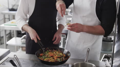 caucasian male chef instructing trainee male chef in kitchen, slow motion