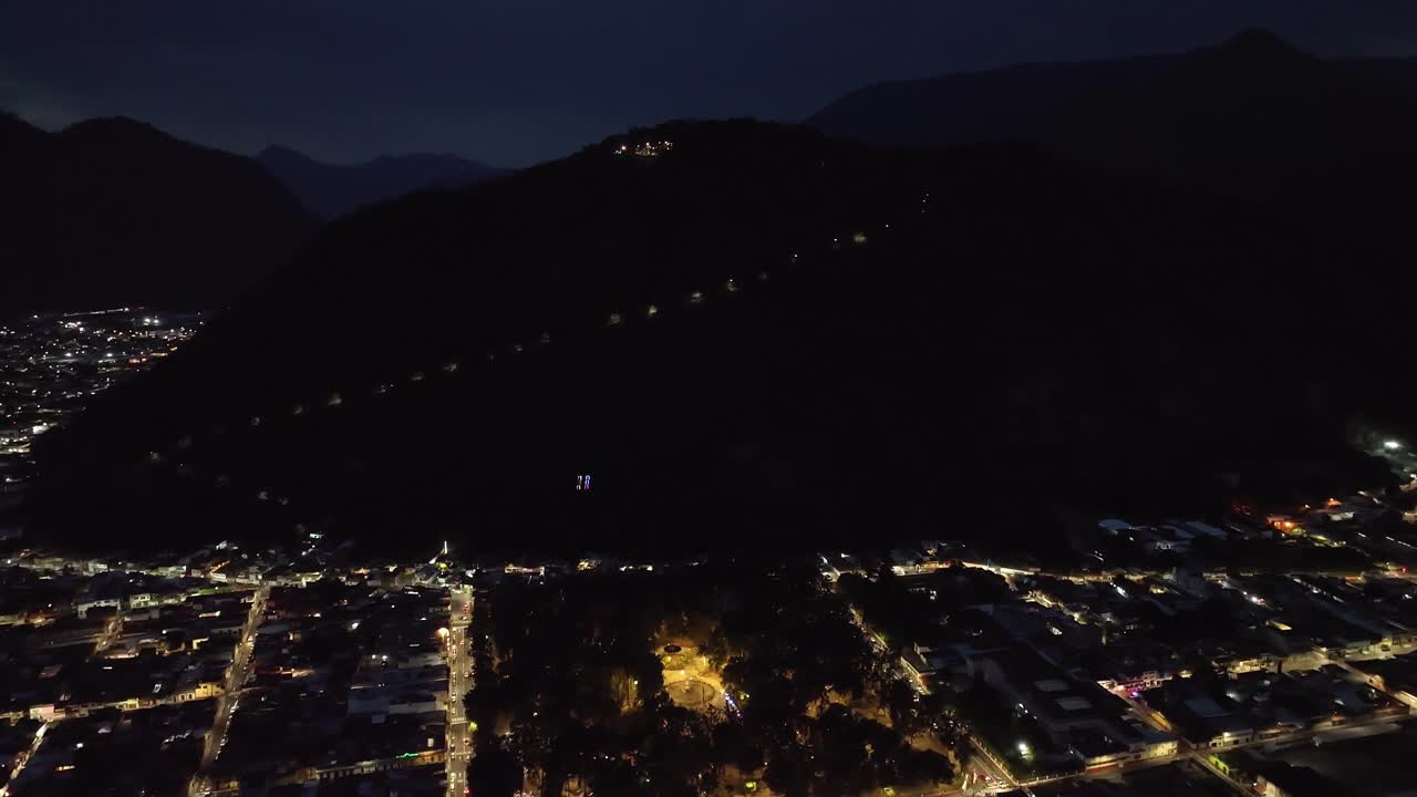 Drone descends above Orizaba, Veracruz, revealing Cerro del Borrego amid dark hills and glowing street grid. Moody nighttime aerial perfect for travel, tourism or cinematic cityscape projects.