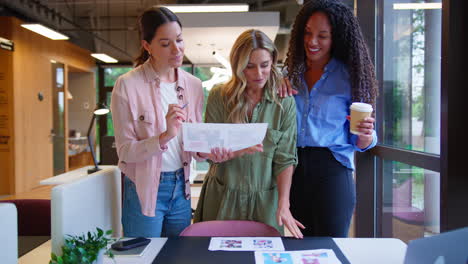 Female-Business-Team-Meeting-At-Desk-In-Open-Plan-Office-Approving-Checking-Proofs-Or-Design-Layouts