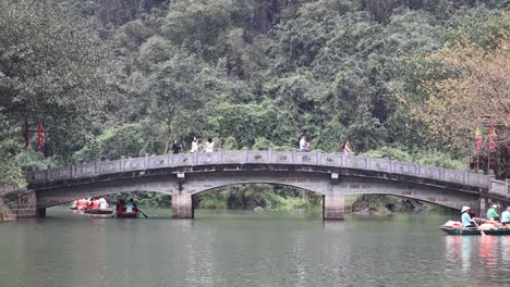 boats passing under a bridge in a lush setting