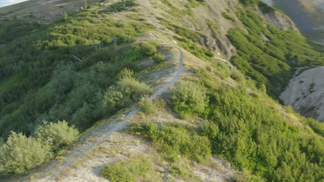 two mountainbikers walking uphill on gravel path ridge in mountains, aerial