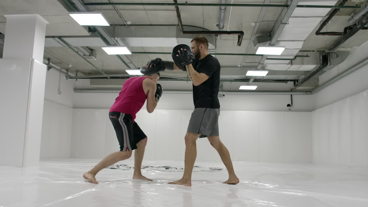 느린 움직임: 권투 발에 힘의 타격. 스포츠 의복에 강한 문신 운동 선수는 파트너와 함께 권투 손에 훈련