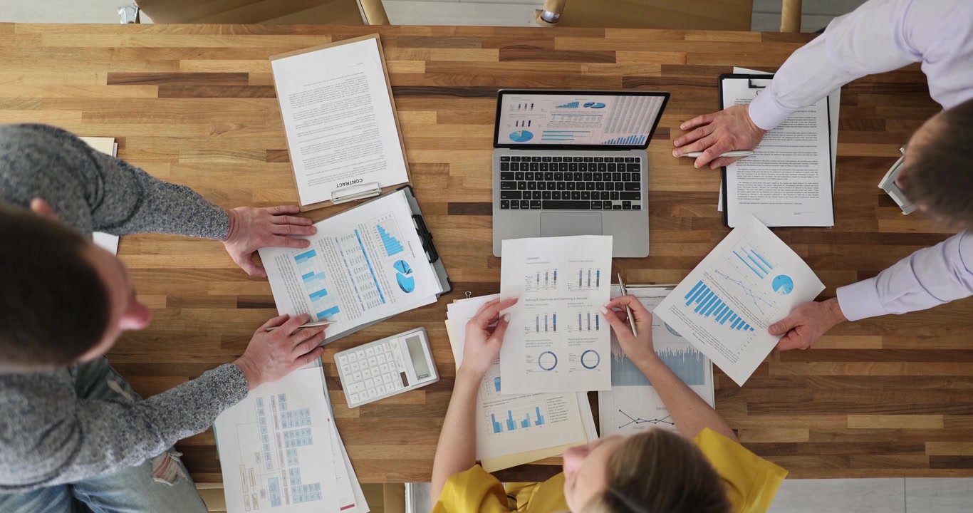 Businesspeople analyze diagrams working on laptop at board table