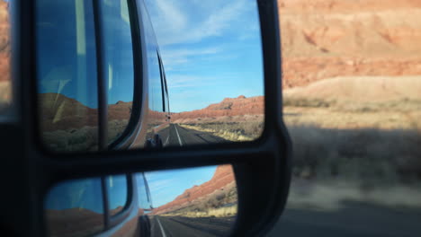 ángulo-Del-Espejo-Retrovisor-De-La-Camioneta-Camper-Del-Desierto,-La-Carretera-Y-El-Cielo-Azul-Durante-Un-Viaje-Por-Carretera-A-Campo-Traviesa