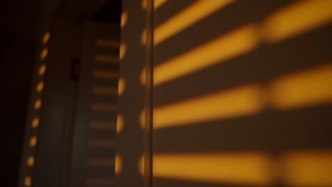 shadow of mechanical rolling window blinds or shutters rolling down on wall. orange colored sunlight in afternoon or early morning shining through window cracks as they shut down creating shadows