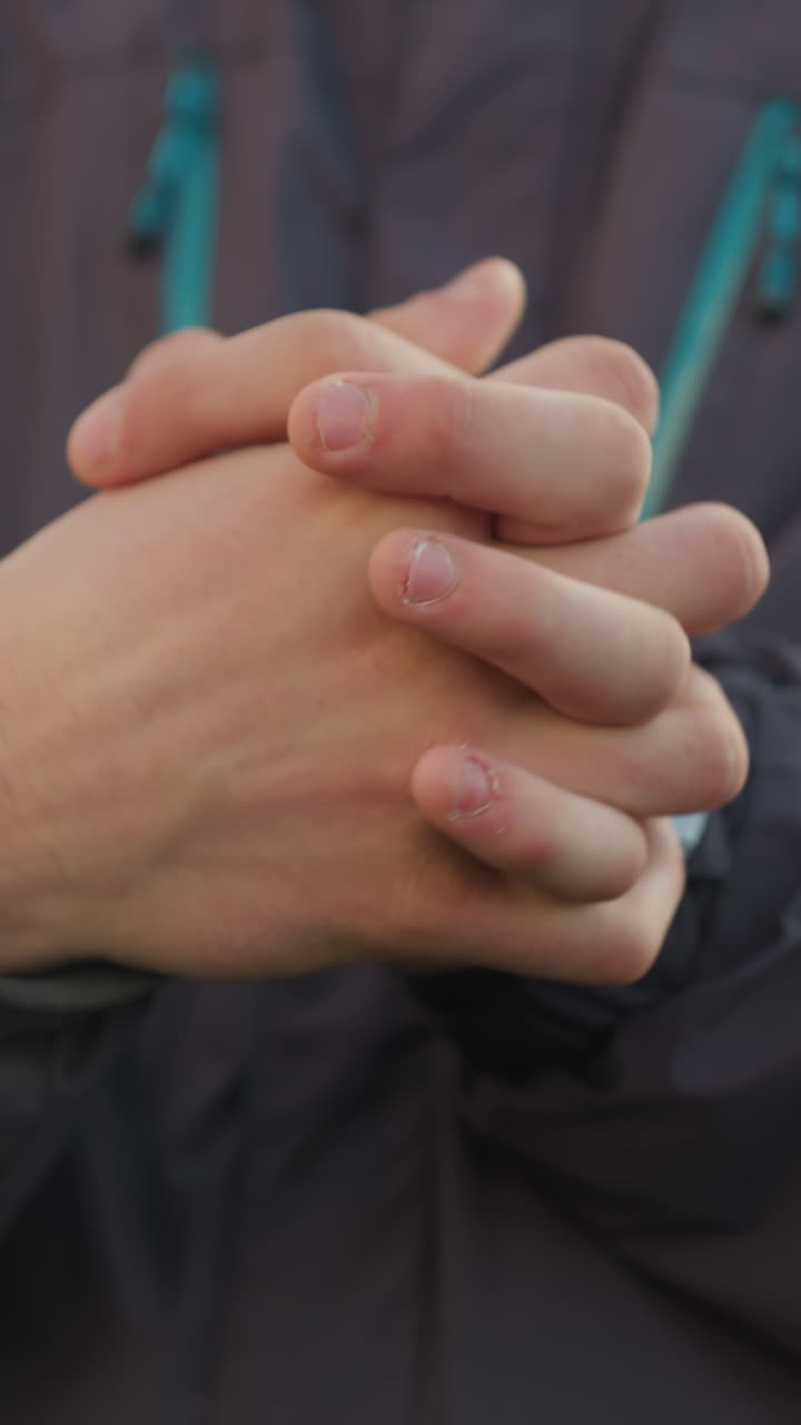 primer plano de manos apretadas estrechamente en contemplación reflexiva, dedos entrelazados con piel visible, sobre un fondo borroso con edificios urbanos y luz natural suave