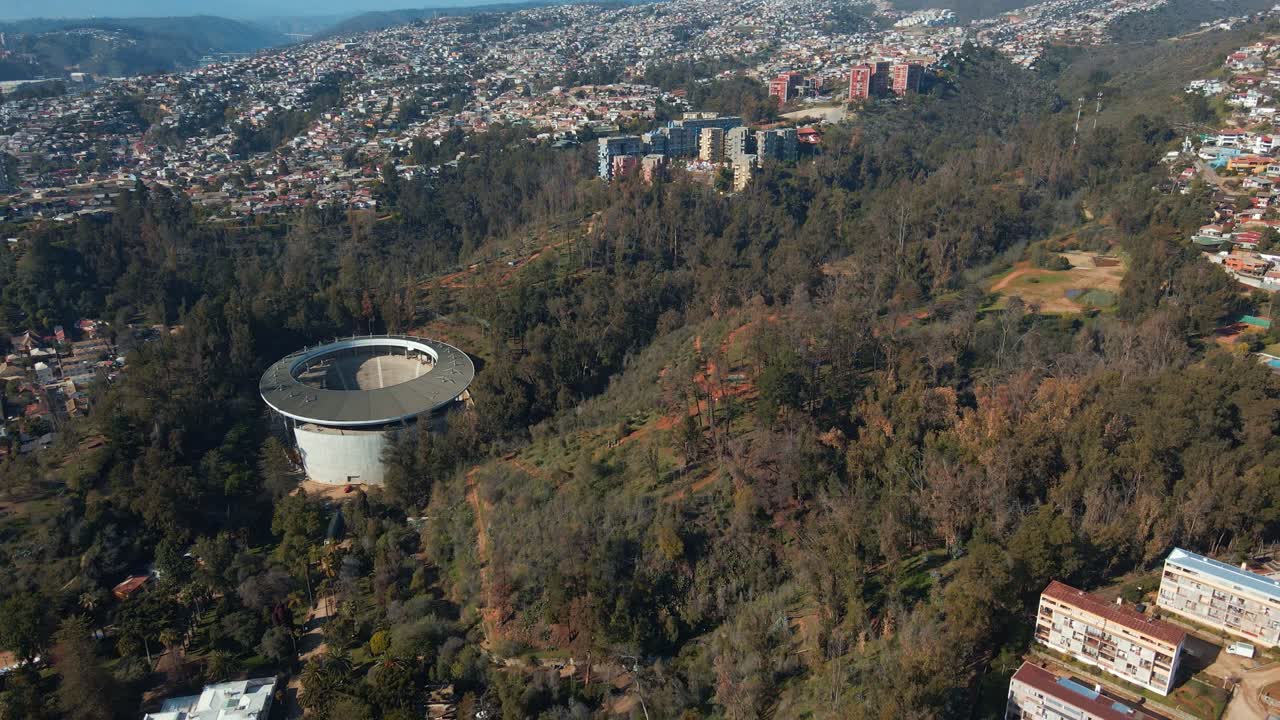 Dolly aereo in allontanamento dall'Anfiteatro Quinta Vergara in un parco ricoperto di boschi, con la città collinare di Viña del Mar sullo sfondo, Cile.