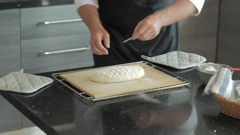 a baker in a clean modern kitchen scores raw artisan bread to allow it to expand during baking