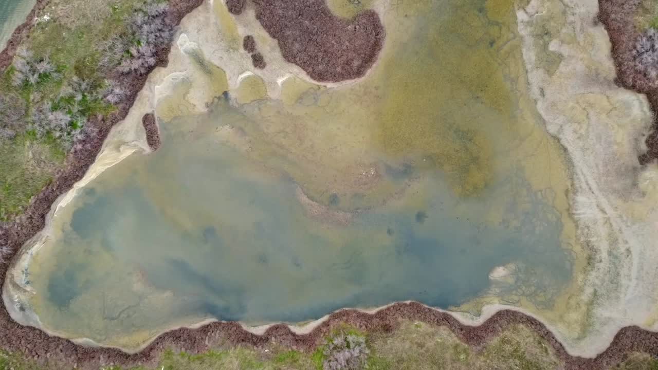Cinematic top-down drone descending shot over a small coastal lagoon pond. High-angle view of unique water patterns and organic shapes. No audio. Ideal for nature and geography storytelling