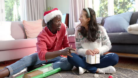 happy diverse couple sitting on floor at home wrapping christmas gifts, slow motion
