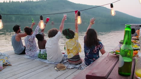 friends toasting with drinks on wooden pier at lake party