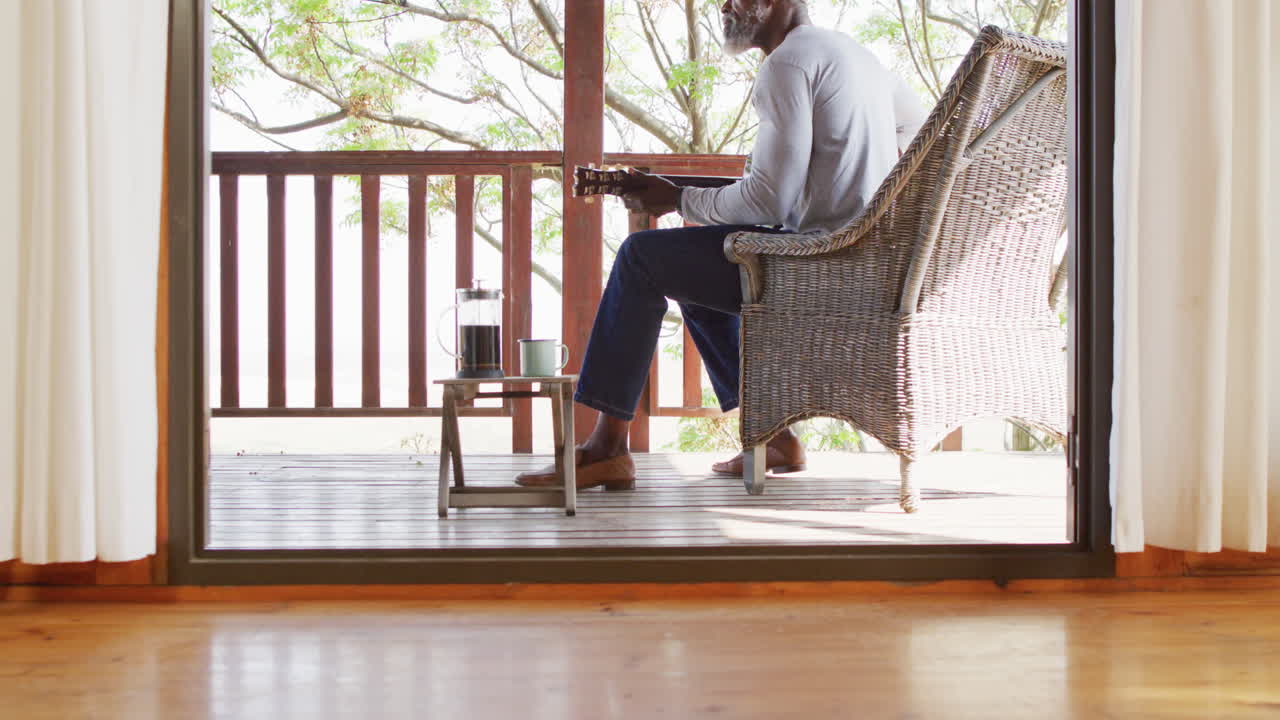 Senior African American man plays guitar on cabin balcony in slow motion