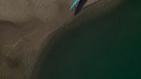 Birdseye-view-of-water-lapping-on-sand-with-outrigger-canoe-laying-down