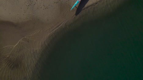 Vista-De-Pájaro-Del-Agua-Lamiendo-En-La-Arena-Con-Una-Canoa-De-Apoyo-Por-La-Que-Se-Establecen