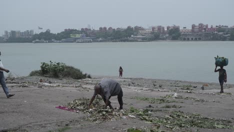 people scavenging and collecting waste on a polluted riverbank in urban india