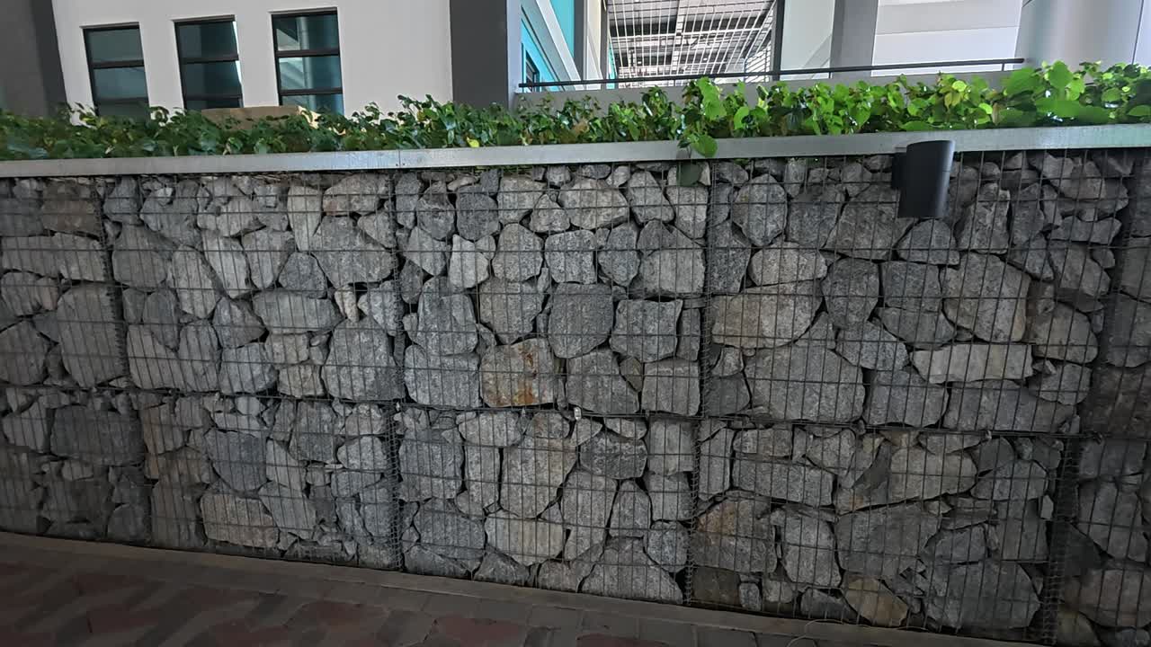 A gabion retaining wall provides structural support and erosion control. The wired cages are filled with rocks, showcasing a durable civil engineering solution