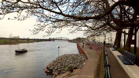 urban countenance landscape time lapse with people strolling by and relaxing along the river ijssel embankment of hanseatic dutch city zutphen with water and recreational boats passing by