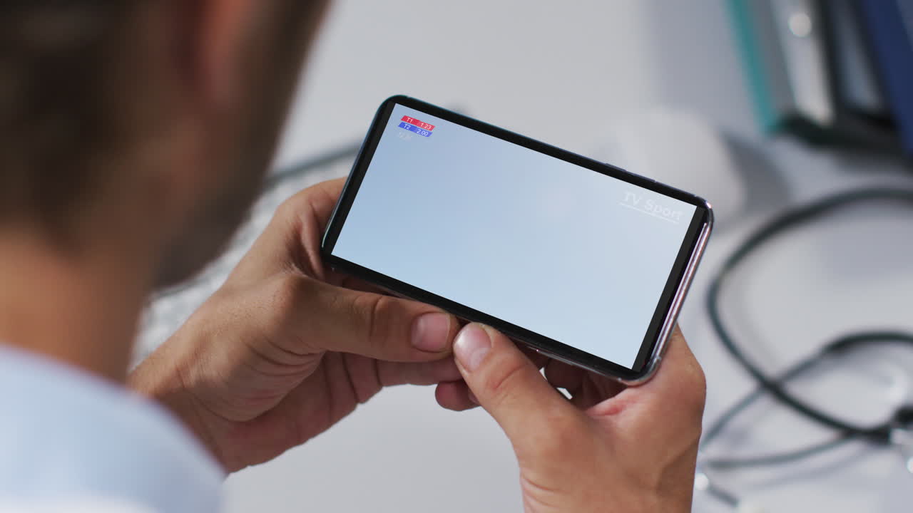 compuesto de un médico masculino viendo un partido de fútbol en un teléfono inteligente