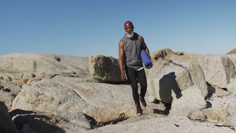 hombre afroamericano de edad avanzada haciendo ejercicio caminando sobre rocas junto al mar