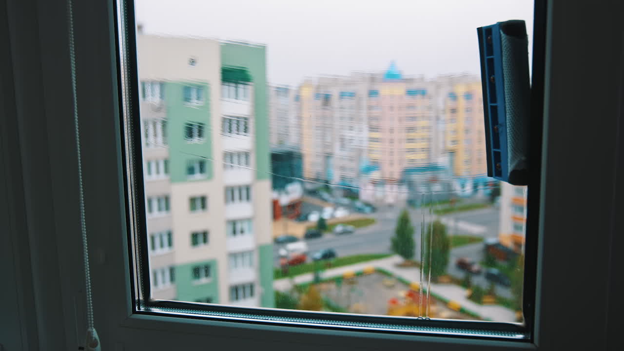 Washing window in the city flat. Man worker cleaning window with a special brush using water on the city background.