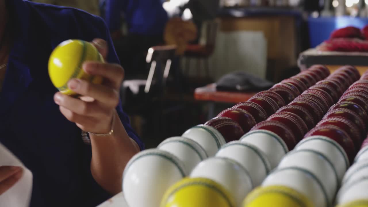Mixed race worker cleaning cricket ball in factory