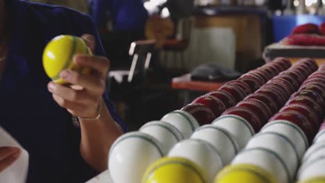 trabajador de raza mixta limpiando una pelota de cricket en una fábrica