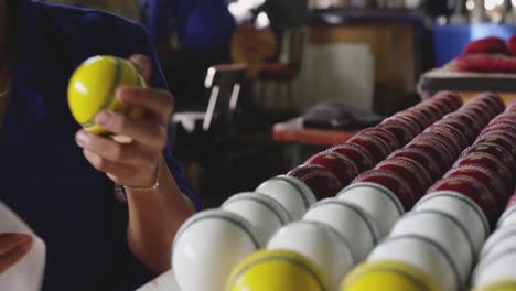 mixed race worker cleaning cricket ball in factory