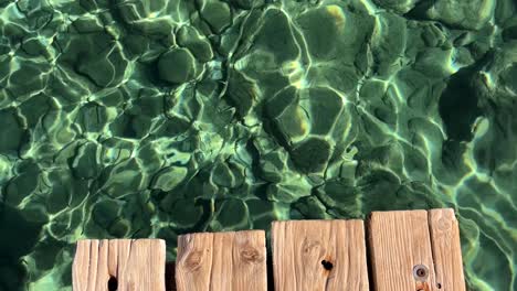 detail of a wooden deck above transparent serene water with fish swimming in crete, greece