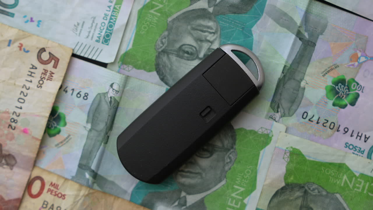 Detailed close-up shot of a car key placed atop Colombian pesos banknotes. Vibrant colors highlight the currency design. Perfect for themes of finance, transport, and economy