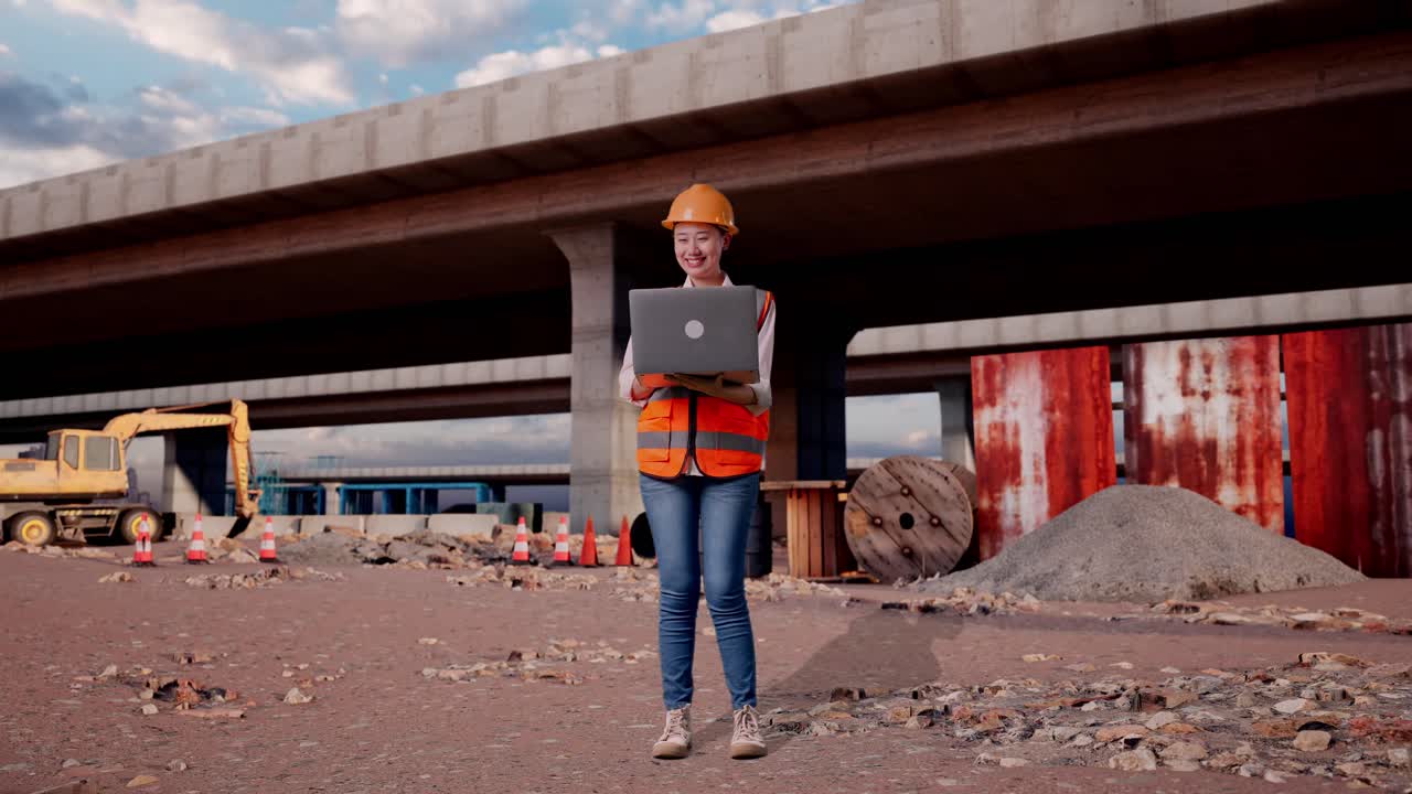 Full Body Of Asian Female Engineer With Safety Helmet Working On A Laptop While Standing At The Site of Highway Construction