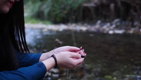 Plano-Medio-De-Una-Hermosa-Mujer-Gótica-Tomando-Agua-Del-Río-En-Sus-Manos