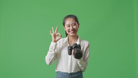 아시아 사진작가 는 스튜디오 에서 녹색 스크린 배경 에 서 있는 동안 카메라 에 있는 사진 을 보고 은 몸짓 을 보여 준다