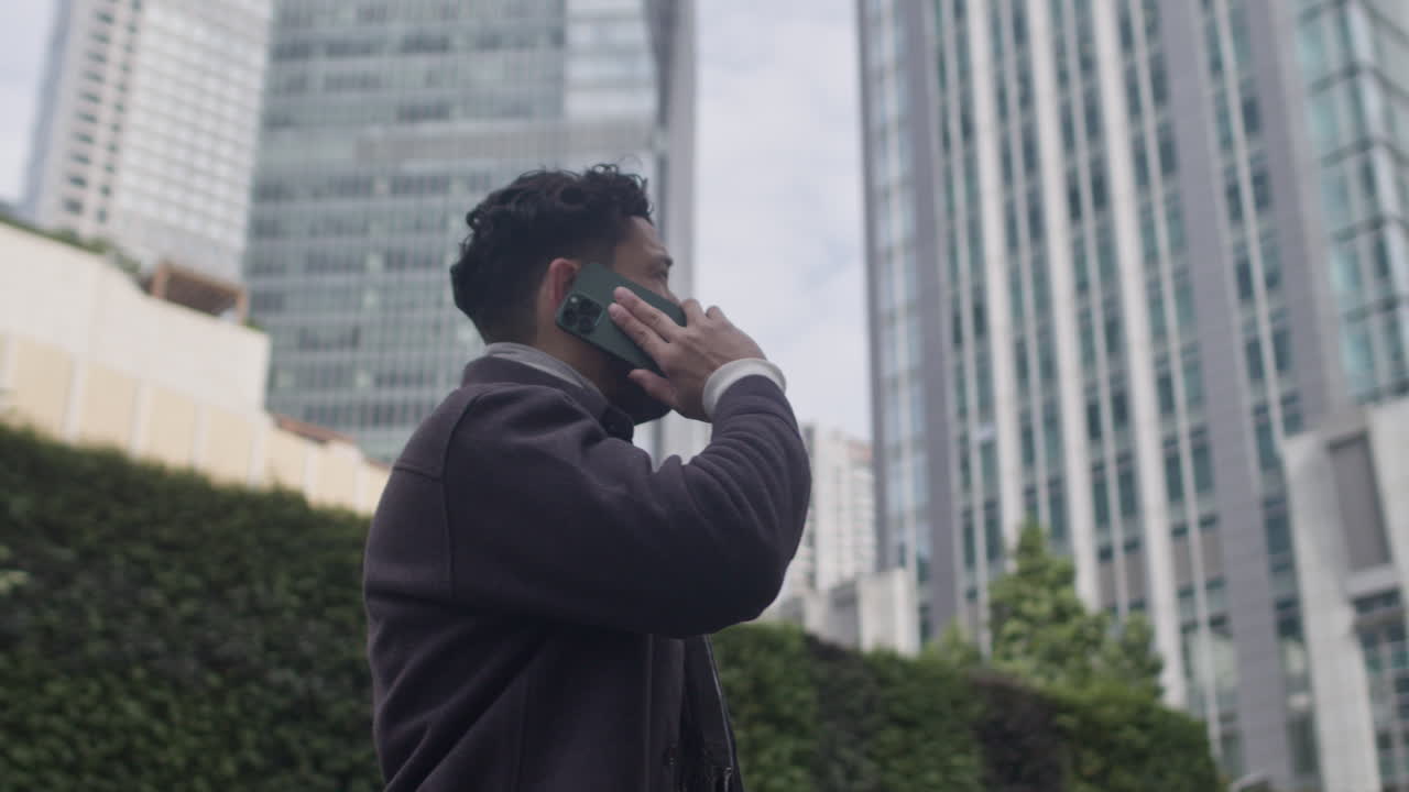 joven apuesto en traje casual de otoño habla por teléfono al aire libre en el distrito de negocios del centro de la ciudad