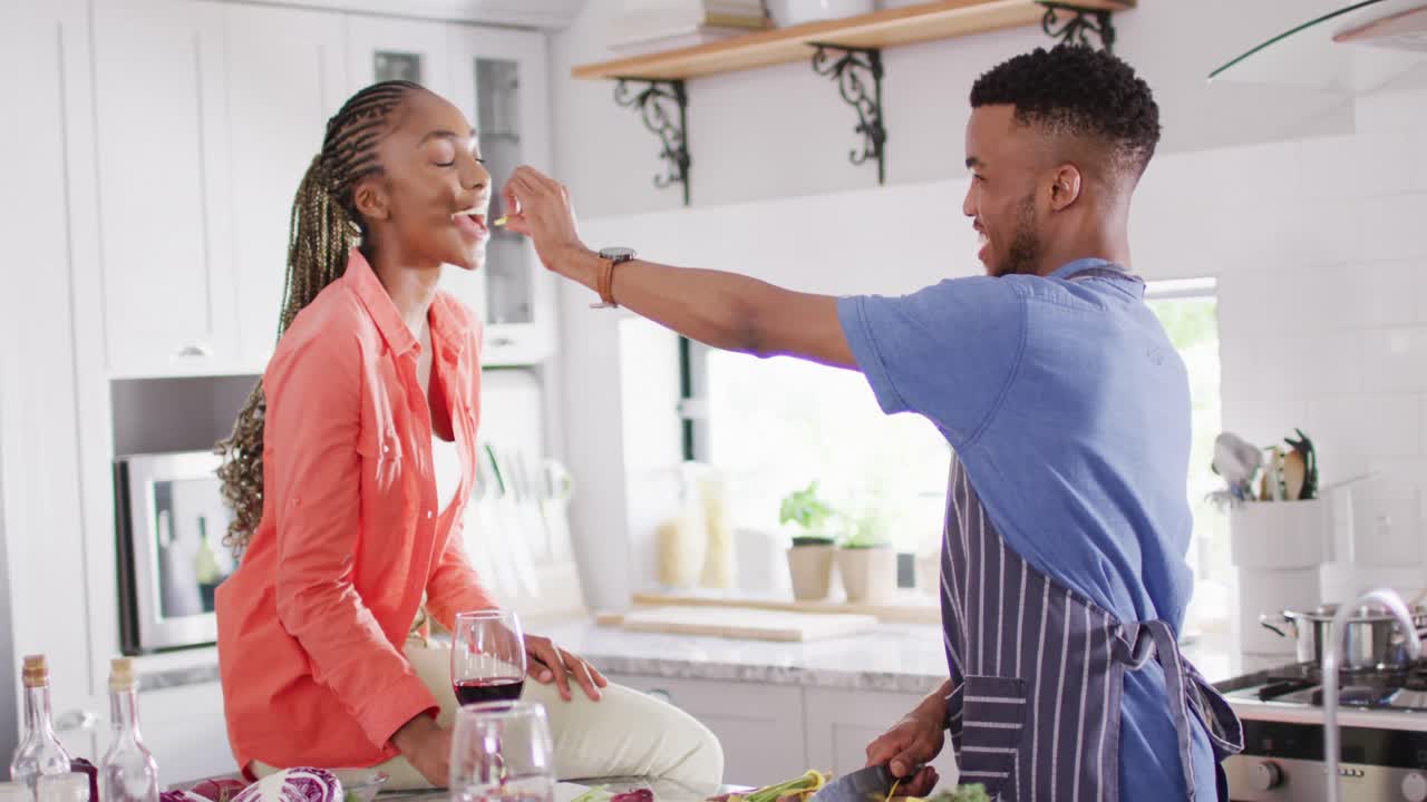 una feliz pareja afroamericana preparando comida en la cocina y probando un plato.