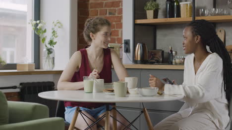 two  female roommates having breakfast and talking together at home