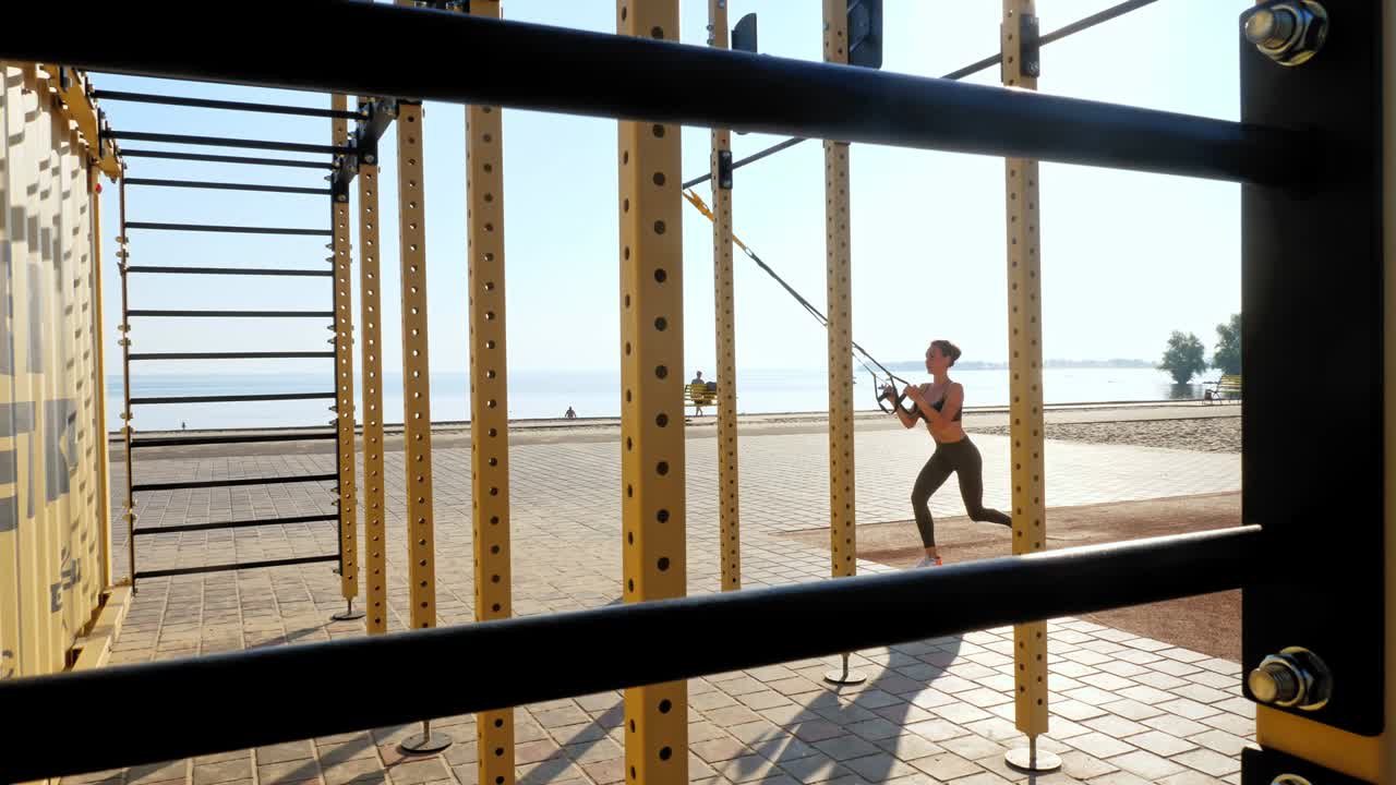entrenamiento al aire libre. correas de suspensión. entrenamiento con correas. mujer joven atlética está haciendo ejercicios de resistencia de todo el cuerpo usando cuerdas en bucle trx, en la playa durante la puesta o el amanecer. entrenamiento de fitness al aire abierto. concepto de estilo de vida saludable. deporte matutino