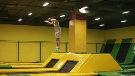 joven atleta masculino con camiseta beige y pantalones cortos salta en el trampolín y disfruta haciendo saltos frontales dobles. juventud, deporte, gimnasia.