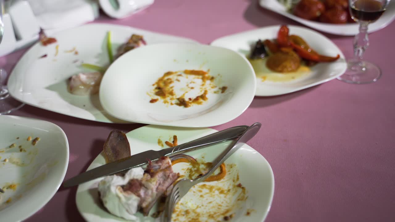 white porcelain plates with remnants of dishes are on a pink tablecloth on the table in the cafe. Camera motion to right