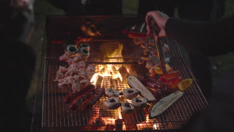 view from behind the shoulders of people on grilling mushrooms, sausage, chicken, eggplant on bbq in front of the house in a garden