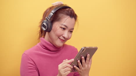 beauty asian gorgeous young woman using a digital tablet and streaming application for happy listening to music on headphones with relaxed on bright yellow background-1