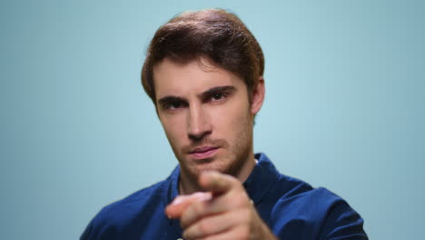 hombre serio señalando con el dedo el fondo azul. hombre confiado posando en el estudio