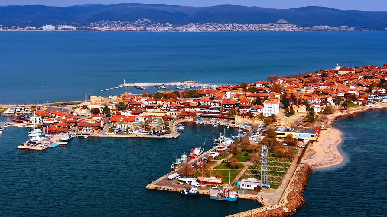 Yoğun kırmızı çatılı mimariye sahip şehrin kıyı kesimi. Güneşli Nessebar, Bulgaristan. Mavi deniz manzarasıyla çevrili. Arka planda sıradağlar
