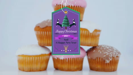 animation of christmas greetings on tag over cupcakes on white background