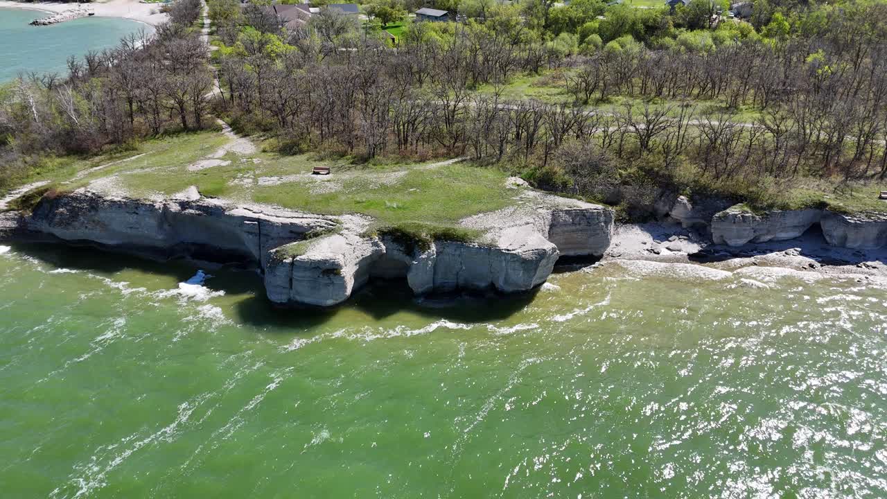 Drone s'élevant tout en étant fixé sur les falaises calcaires de Steep Rock, Manitoba, maintenant la mise au point tandis que les eaux vertes du lac Manitoba, le rivage et les arbres restent visibles par une journée d'été