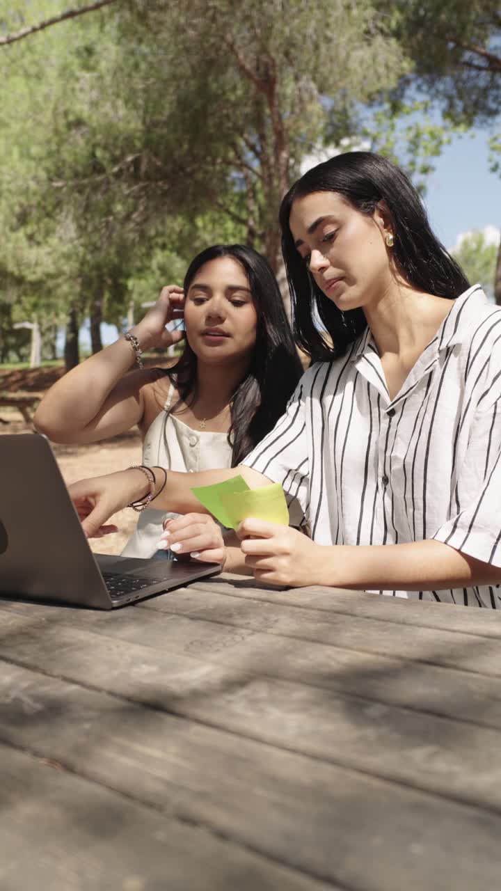 Two women working on a laptop outdoors at a picnic table
